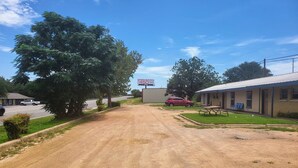 A rural road leading to a motel with a dirt driveway, a red car parked, and a large billboard in the background.