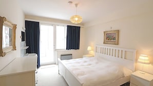 Ein Hotelzimmer mit Bett, Nachttischen, einer Lampe, einem Fenster mit Vorhängen, einem Heizkörper und einem Spiegel.
