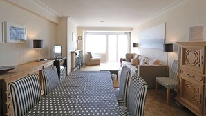 Ein Wohnzimmer mit einer Couch, Sesseln, einem Esstisch mit Stühlen, einem Fernseher und einem Kamin.