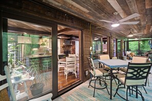 A dining area with a table and chairs, a ceiling fan, and a view of the kitchen through glass doors. - Modern, Luxurious Cabin for Two located on a Cascading Waterfall. (Jasper)