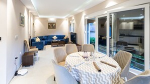 A modern living room with a dining area, a sofa set, a TV, and a glass door leading to a balcony. - Villa Tomi Nature Retreat (Sarajevo)