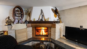A fireplace with a fire, a television, and various hunting and fishing tools on the mantel. - Villa Tomi Nature Retreat (Sarajevo)