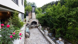 A stone pathway leading to a stone fireplace with a chimney, surrounded by lush greenery and a small stream. - Villa Tomi Nature Retreat (Sarajevo)