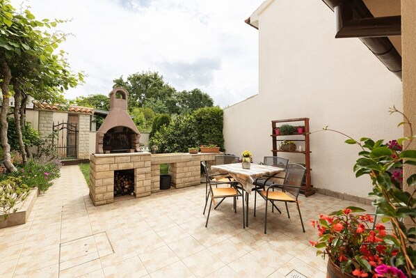 An outdoor patio with a stone barbecue area, a table with chairs, and potted plants.
