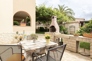 An outdoor patio with a table and chairs, surrounded by potted plants and a stone oven.