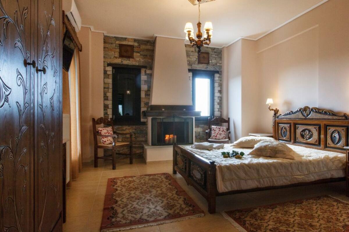A bedroom with a stone fireplace, a bed with ornate headboard, a wooden wardrobe, and two rugs.
