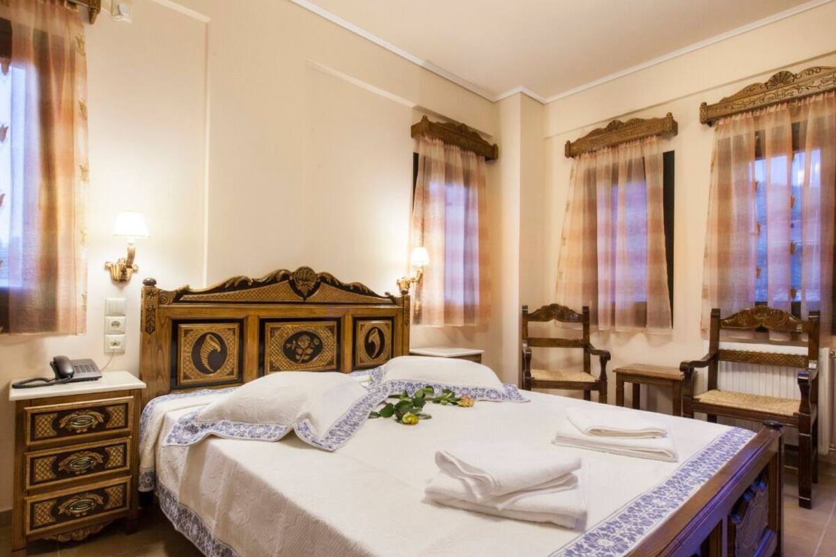 A hotel room with a large bed, wooden headboard, two bedside tables, a nightstand, and a chair.