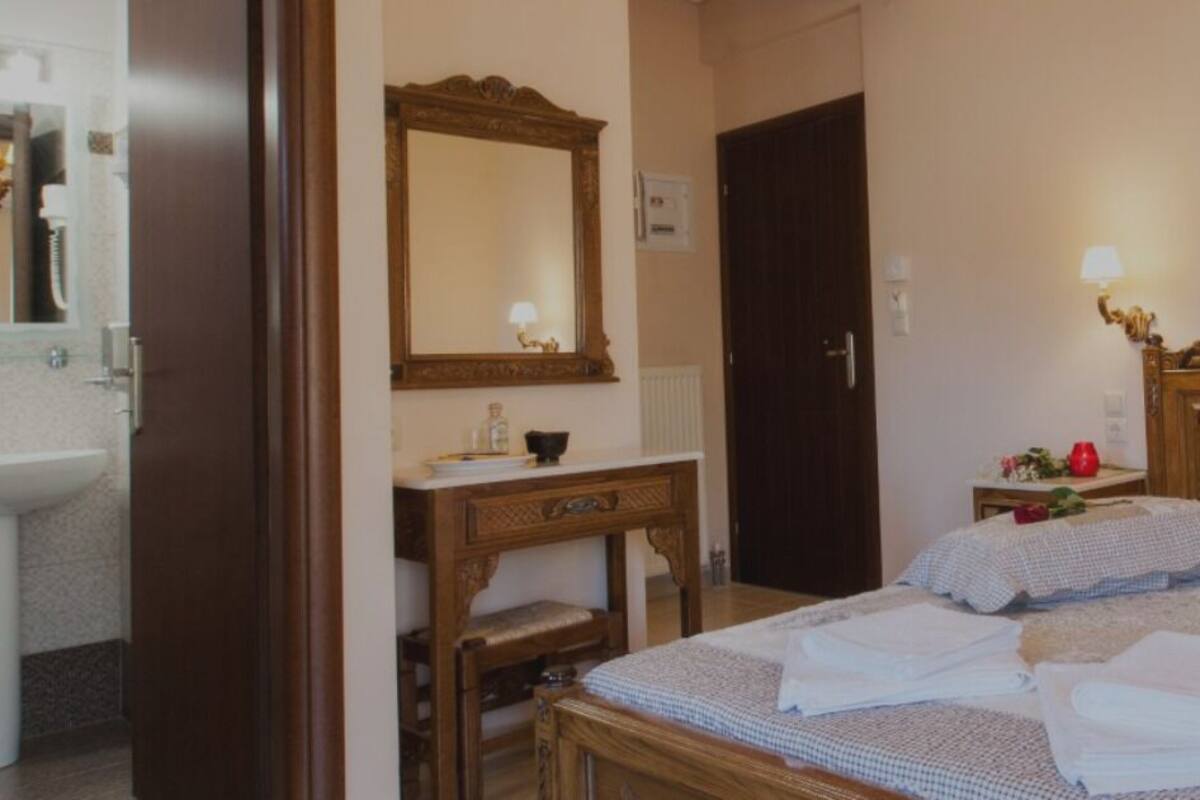 A hotel room with a wooden bed, two bedside tables, a nightstand, a mirror, a sink, and a small table with a vase of flowers.