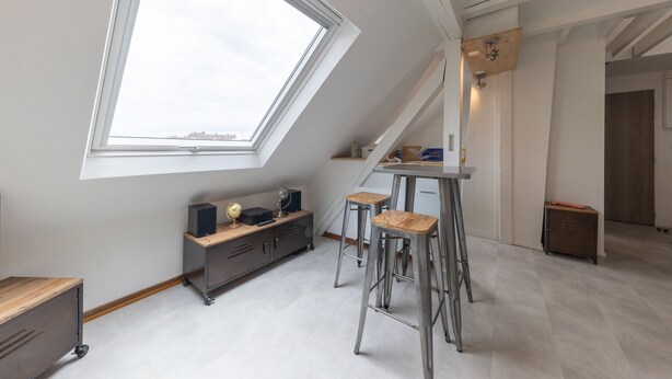 A modern loft bedroom with a skylight, a desk, and a small kitchenette.