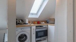 A compact kitchen with a washing machine, oven, and a skylight.
