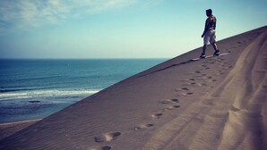 A person standing on a sandy beach with footprints leading towards the ocean.