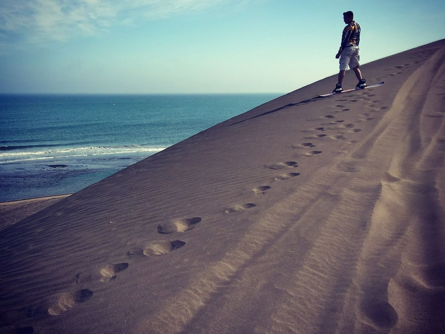 A person standing on a sandy beach with footprints leading towards the ocean.