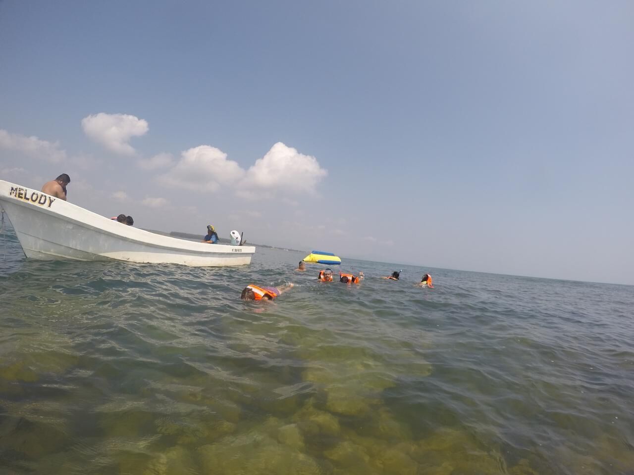 Un bote llamado 'MELODY' con gente nadando en el agua.