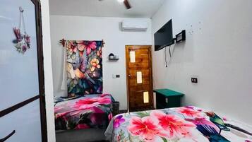 Una habitación con dos camas, ventilador de techo, televisor y una puerta.