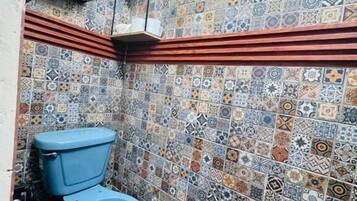 Un baño con inodoro azul, baldosas estampadas y suelo de madera.