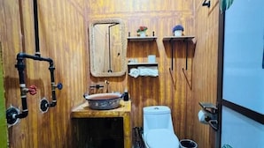 A small bathroom with a wooden wall, a white toilet, a sink with a mirror, and a shower area.