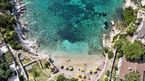 An aerial view of a coastal area with clear turquoise waters, a sandy beach, and a park with yellow umbrellas. - Miromara Hotel Karaburun (Karaburun)
