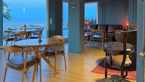 A spacious room with a large window overlooking the ocean, a dining area with wooden furniture, and a seating area with leather sofas. - Miromara Hotel Karaburun (Karaburun)