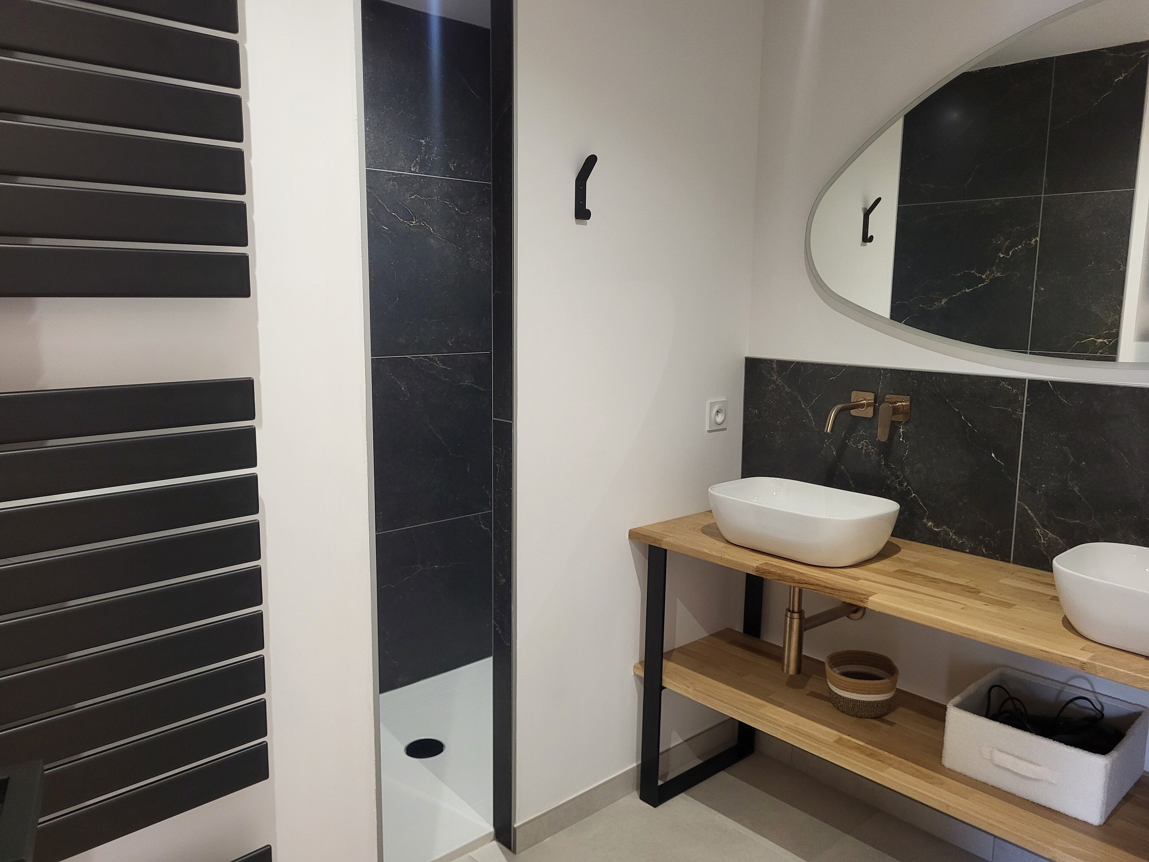 A modern bathroom with a black and white tiled wall, a wooden vanity with a white sink, and a mirror above the sink.