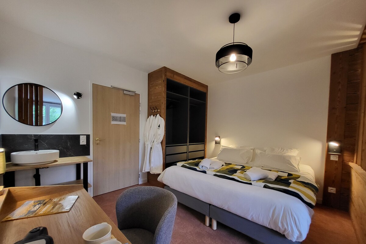 Habitación de hotel con cama, mesita de noche, silla y un espejo grande.