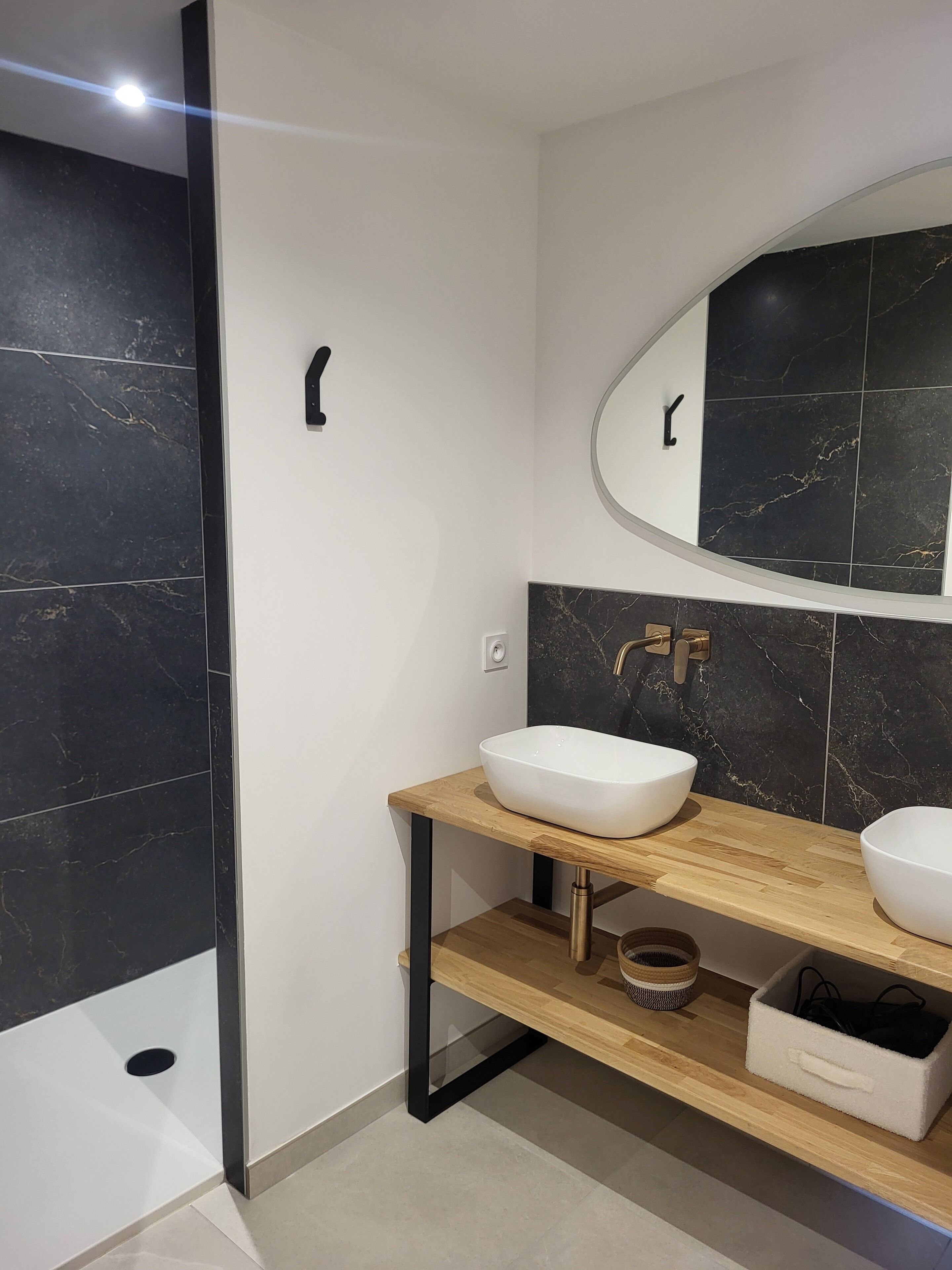 Ein modernes Badezimmer mit zwei weißen Waschtüben, einem hölzernen Waschtisch, einem großen Spiegel und schwarzen Marmorfliesen.