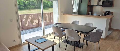 A modern kitchen with a central island, a dining area with a table and chairs, and a sliding glass door leading to an outdoor patio.