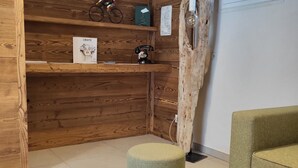 Una habitación con paredes de madera, un taburete verde acolchado, un sofá verde y una mesa de madera con una revista.