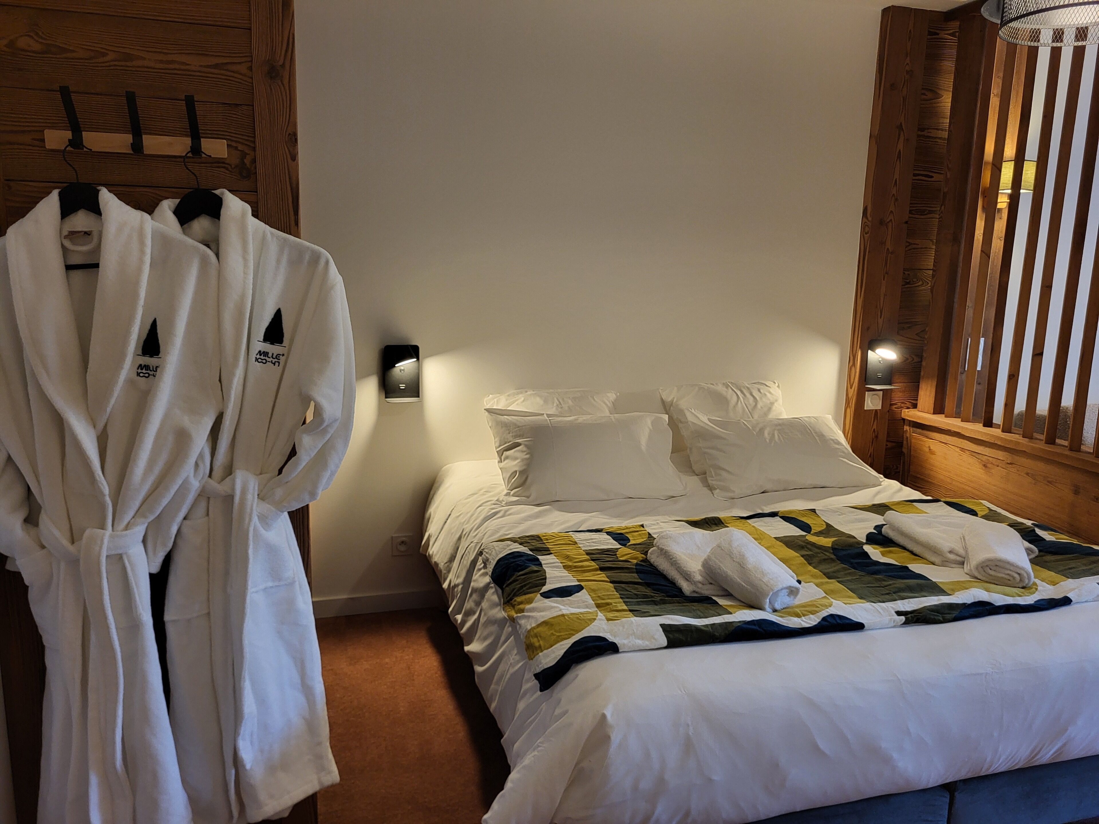 Una habitación de hotel con cama, toallas blancas y un perchero para batas.