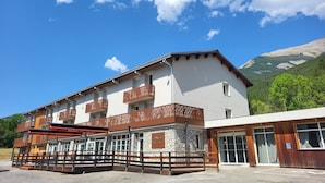 Un hotel de varios pisos con balcones, fachada de piedra y montañas al fondo.