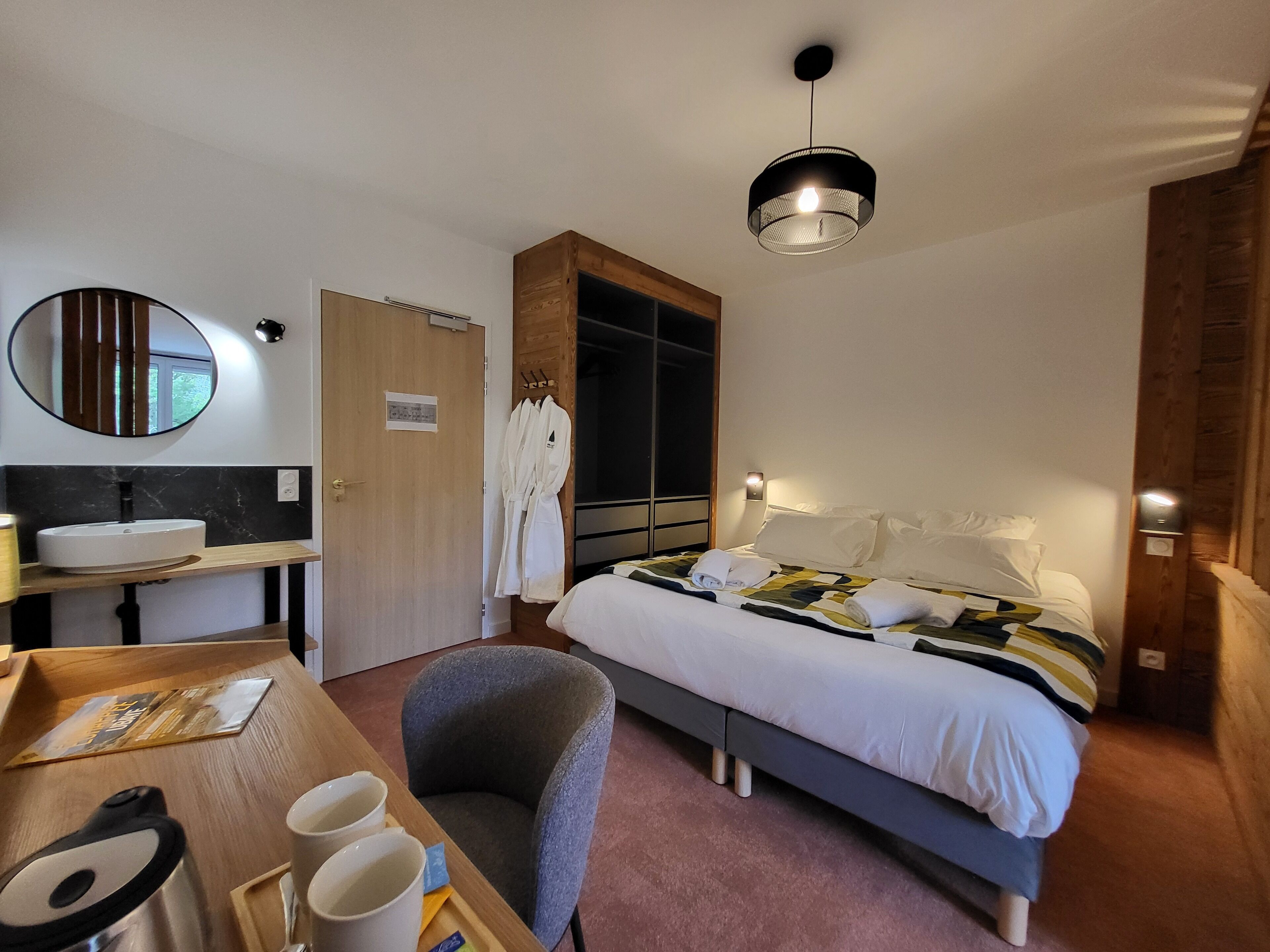 A hotel room with a bed, bedside table, chair, and a large mirror.