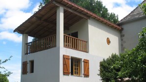 A two-story house with a balcony, stone foundation, and wooden shutters.