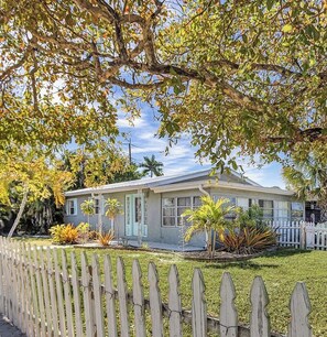 A single-story house with a front porch, surrounded by a wooden fence, and various plants in the yard. - Private entry 1-bedroom suite with Heated POOL & HOT TUB, in lovely Fort Myers  (Fort Myers)