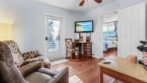 Un salon avec un ventilateur de plafond, un téléviseur, un bureau en bois, une chaise et un canapé.