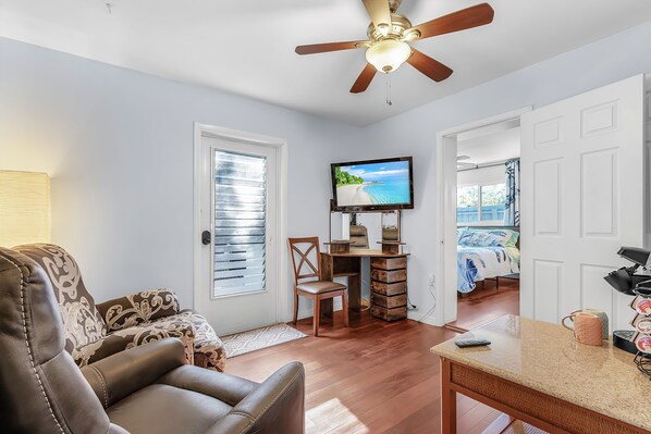 A living room with a ceiling fan, a TV, a wooden desk, a chair, and a couch.