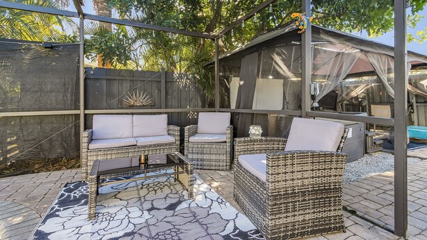 Une terrasse extérieure aménagée avec des meubles en osier, une table en verre et un tapis à motifs.