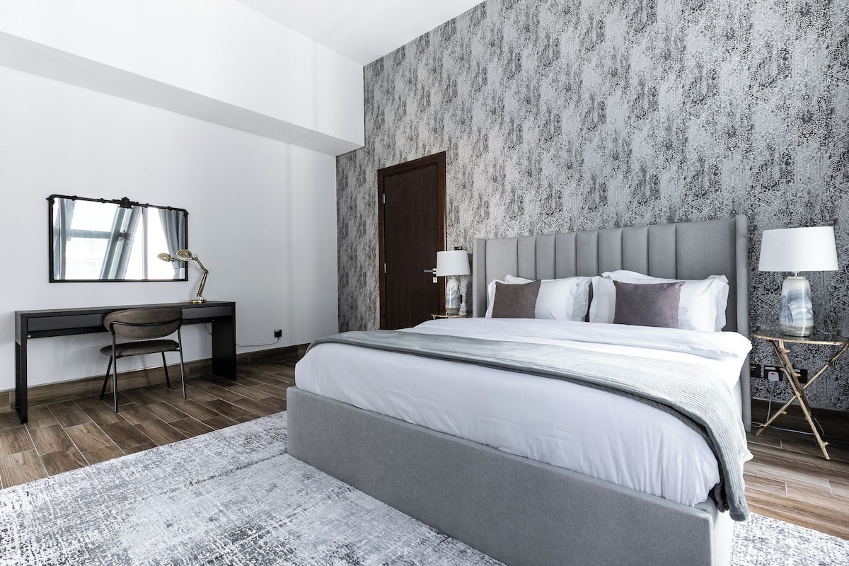 A modern bedroom with a large bed, a desk, and a chair.