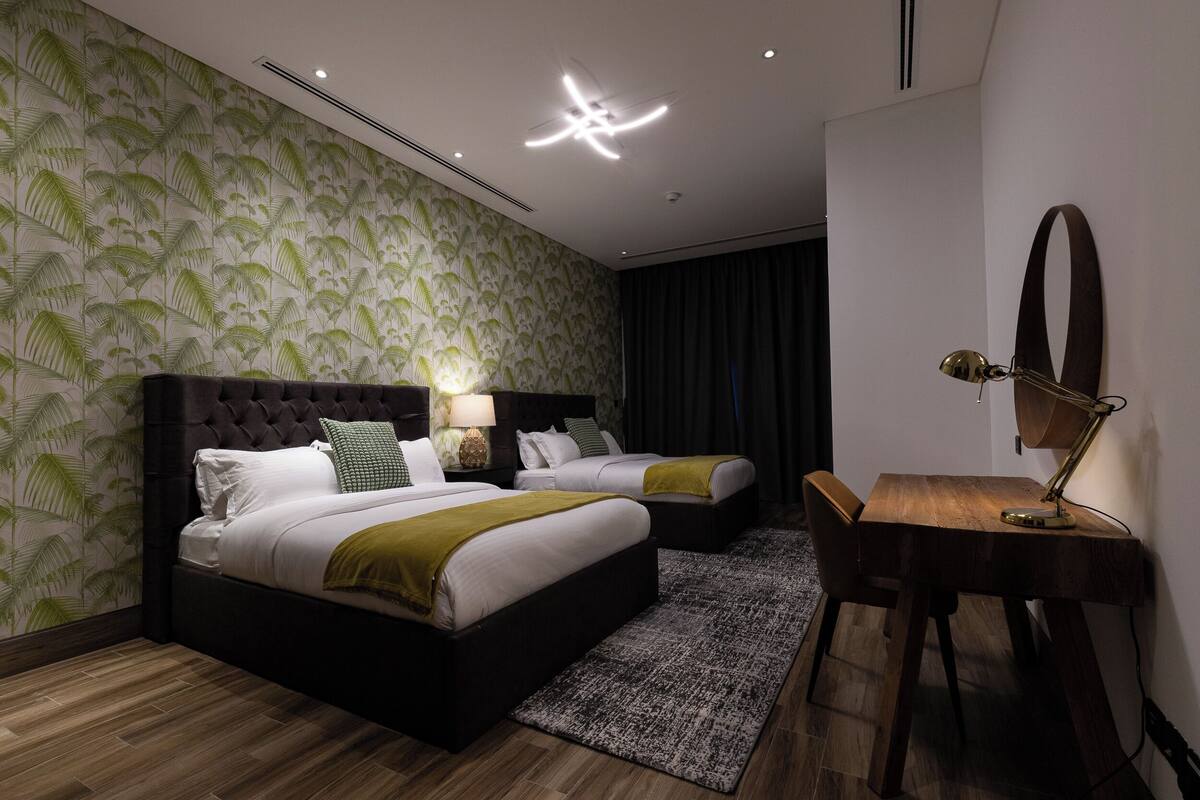 A modern hotel room with two beds, a desk, and a ceiling light fixture.