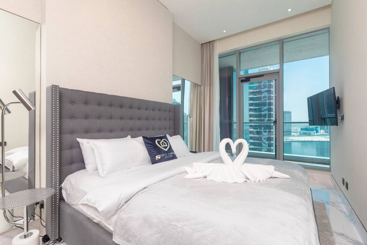 A modern hotel room with a large bed, a view of the city, and a neatly made bed with a swan-shaped pillow.
