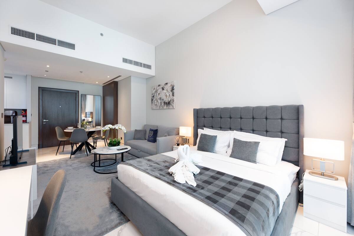 A modern hotel room with a large bed, a seating area with a round table, and a separate dining area.