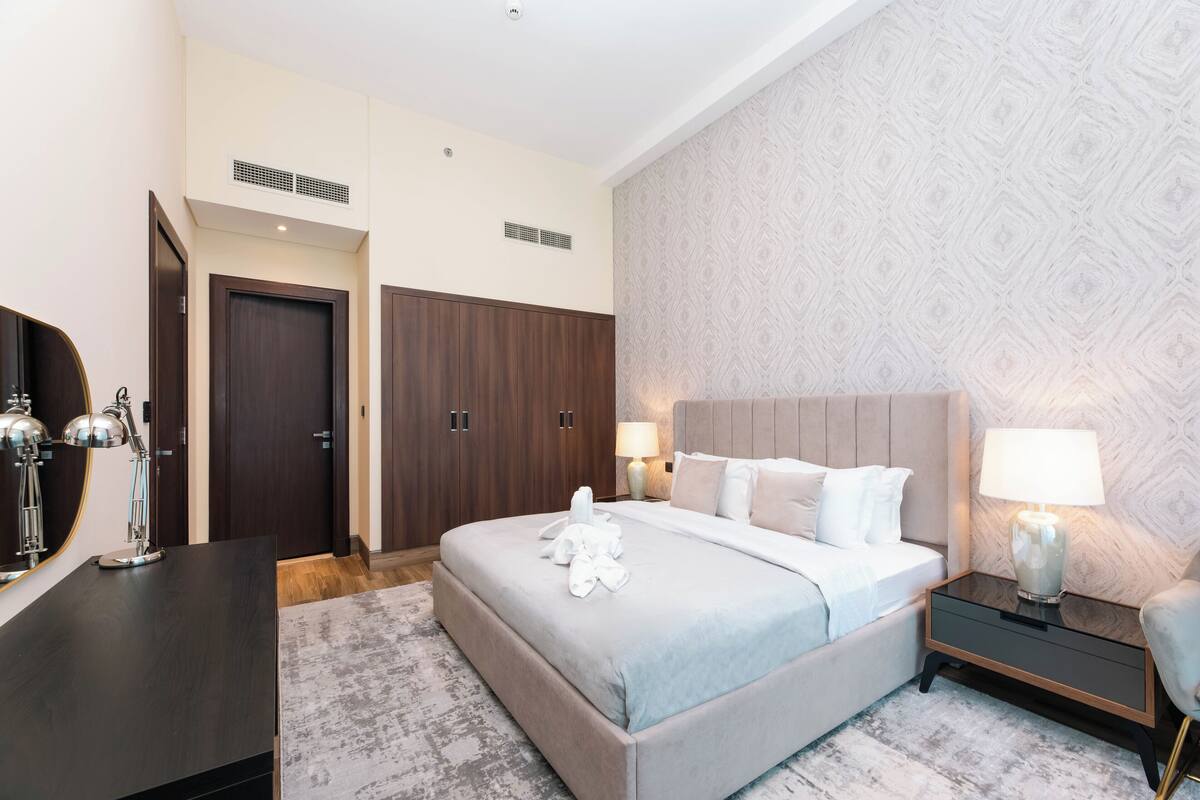 A hotel room with a large bed, bedside lamps, a wooden wardrobe, and a patterned wall.