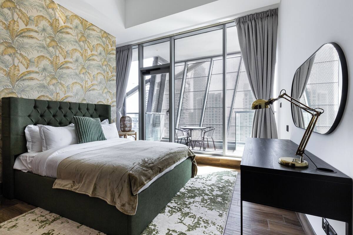 A modern bedroom with a large bed, a desk, and a view of the city through large windows.