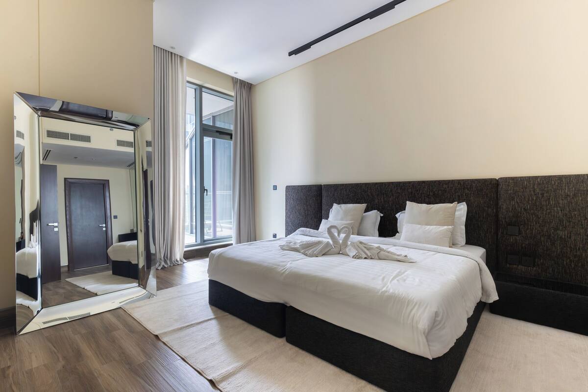 A modern hotel room with a large bed, a mirror, and a view of the outdoors.
