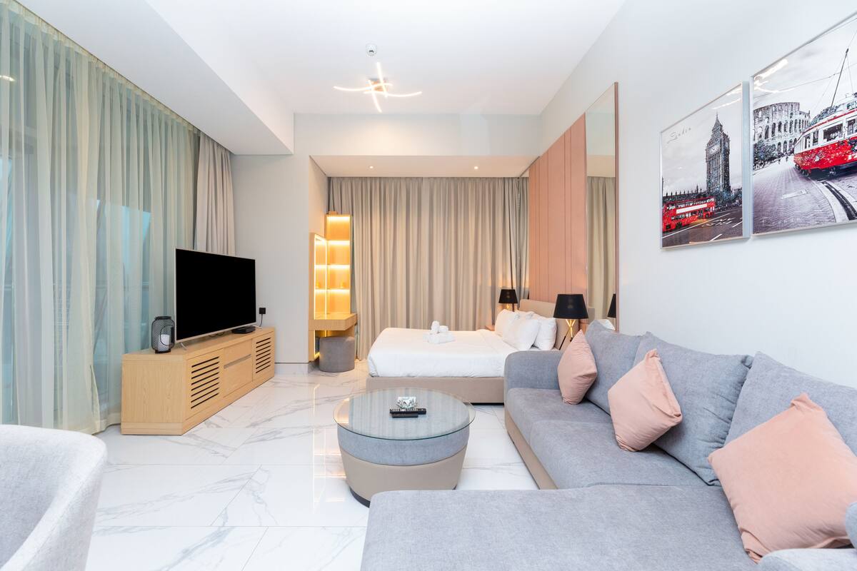 A modern hotel room with a large bed, a sofa, a TV, and a coffee table.