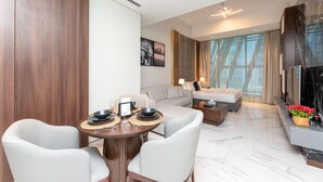 A modern hotel room with a dining area, a sofa, a TV, and a large window. - SIMPLY COMFORT Urban Chic Suites in J One Tower City & Canal Views (Dubai)