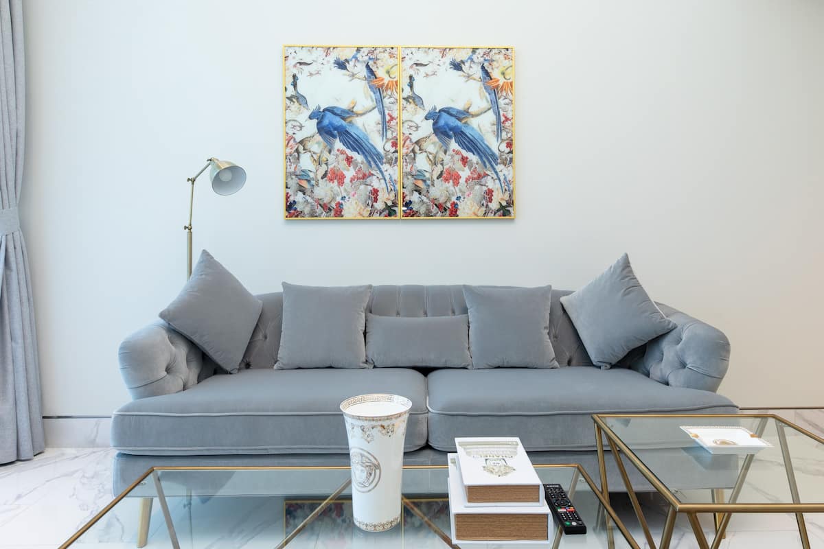 A living room with a grey sofa, a glass coffee table, a floor lamp, and a painting of birds on the wall.