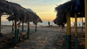 Een strand met rieten parasols en een zandpad dat naar het water leidt.