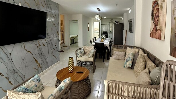 Een moderne woonkamer met een marmeren wand, rieten meubels, een flatscreen-tv en een eethoek met een tafel en stoelen.