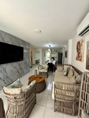 A modern living room with a marble wall, wicker furniture, a flat-screen TV, and a dining area with a table and chairs. - Relaxing Oceanview Home in Cartagena, La Boquilla – Steps from the Beach (La Boquilla)