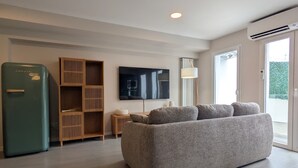 Una sala de estar moderna con un sofá, un televisor, un aparador de madera y una lámpara de techo.