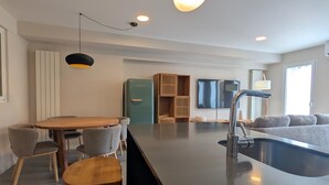 Una cocina moderna con una isla central, horno empotrado y comedor con sillas.